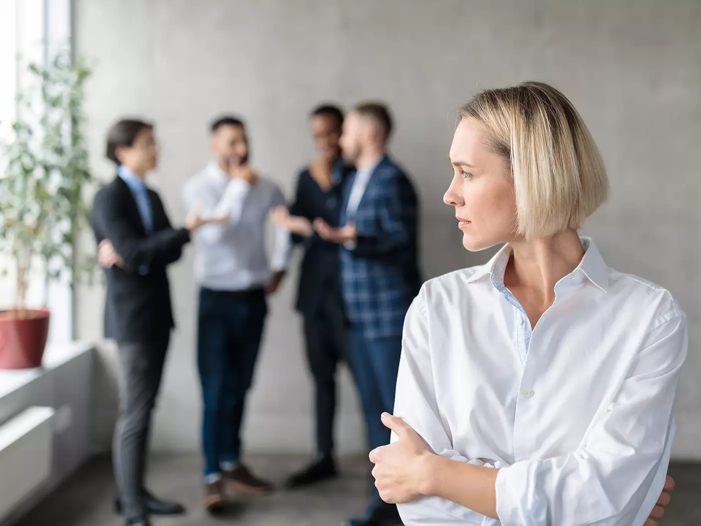 En kvinna framför en arbetsgrupp, kvinnan kan vara chef, ser åt ett annat håll än arbetsgruppen, ser stressad ut, har vit blus.