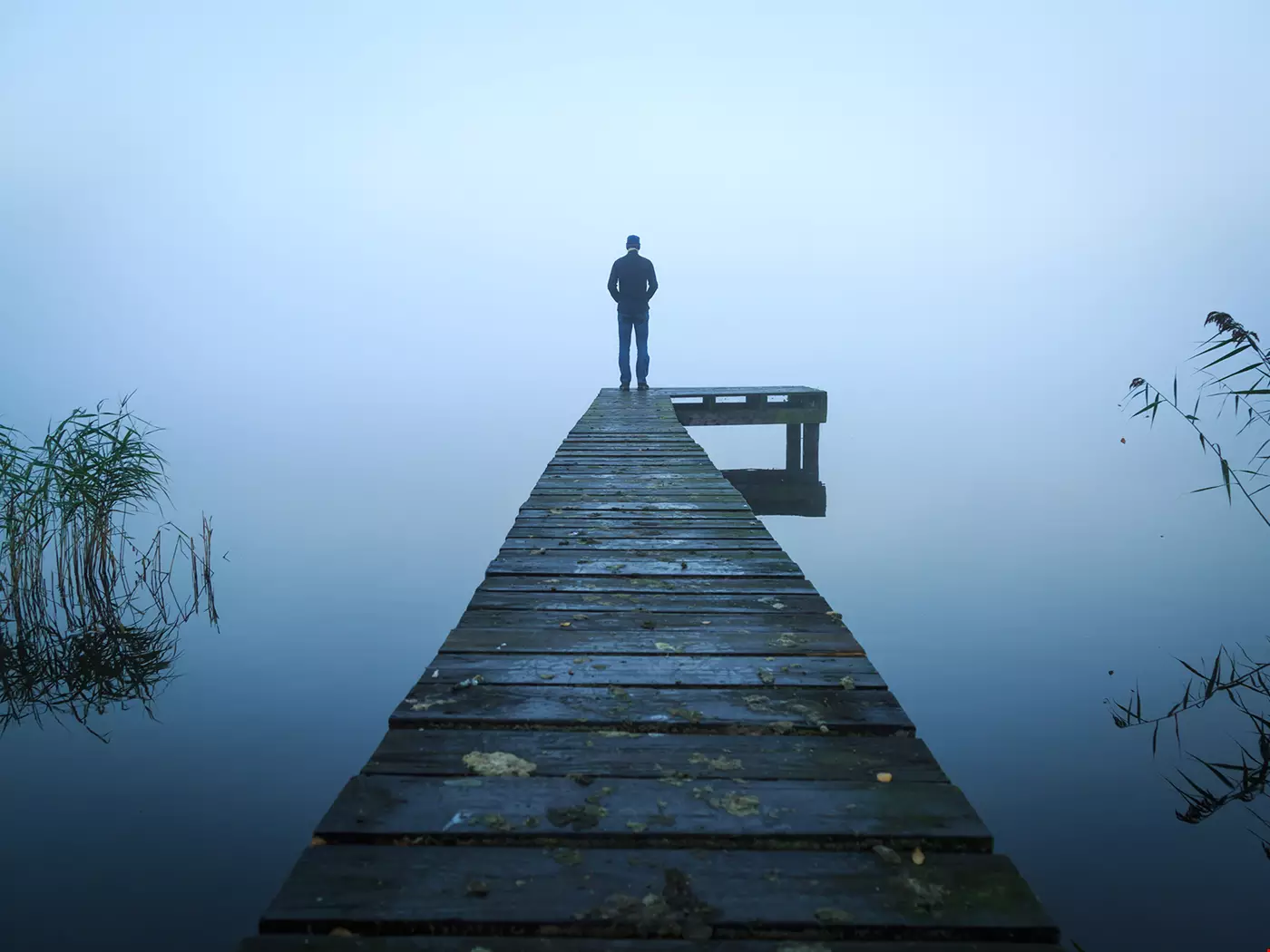 Längst ut vid slutet av en brygga sitter en man med ryggen mot fotografen, det är dimmigt på bilden