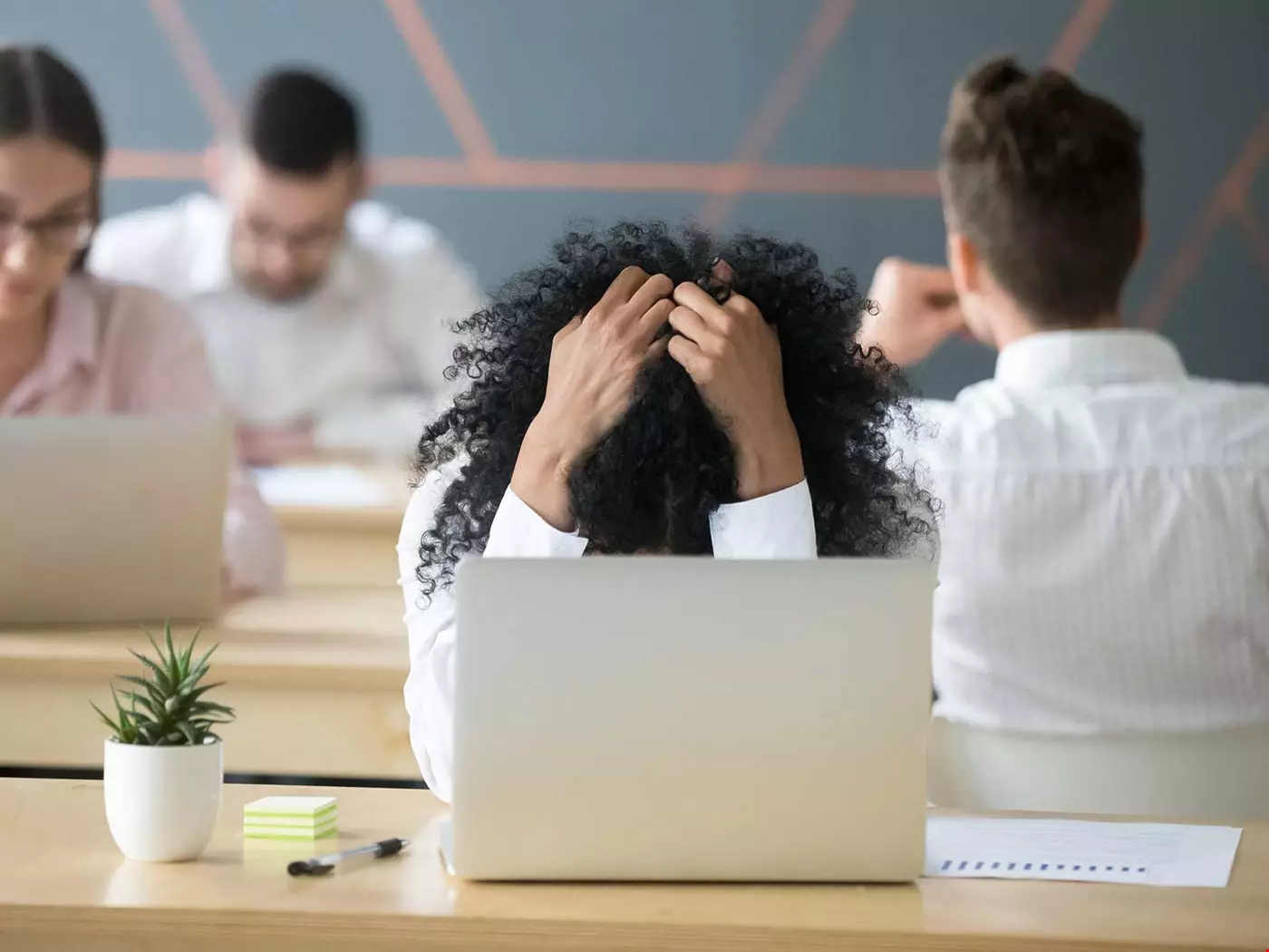 En person, troligen en chef, vid skrivbordet, håller förtvivlad huvudet i händerna, ser stressad ut.