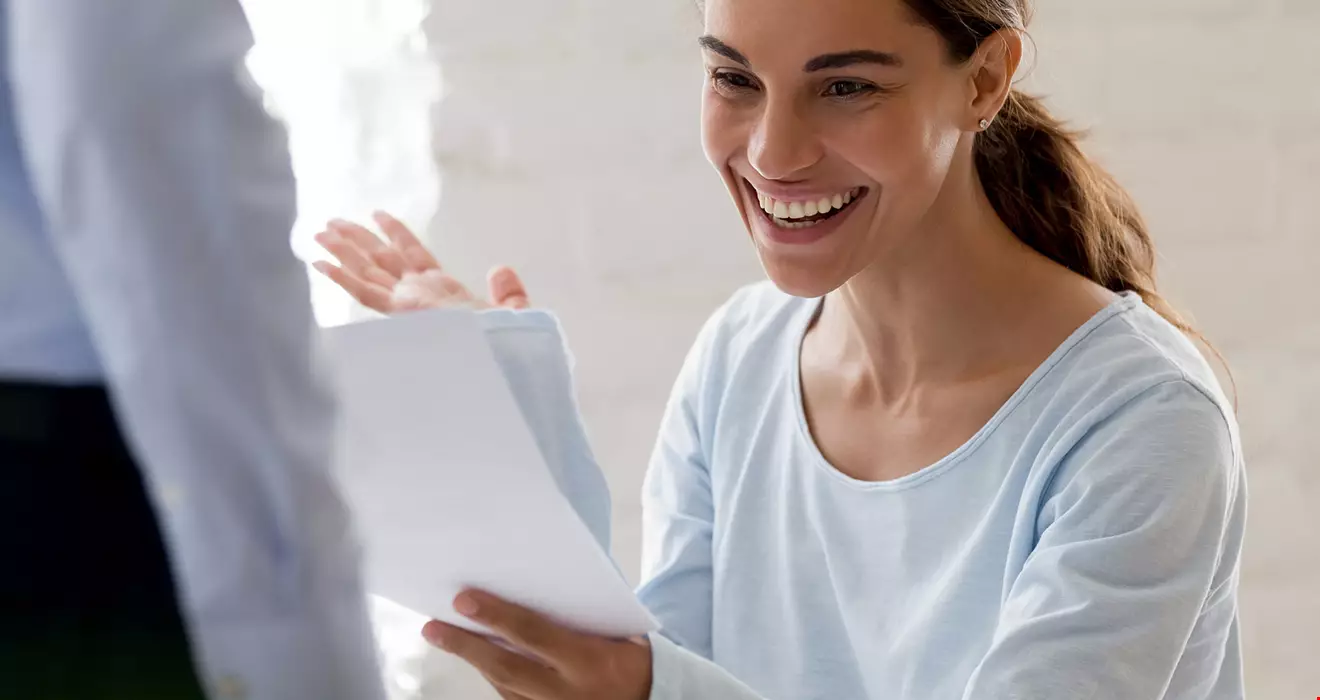 En kvinna tittar på ett papper och ser glad ut, kanske fått ett bra besked Akavia Aspekt