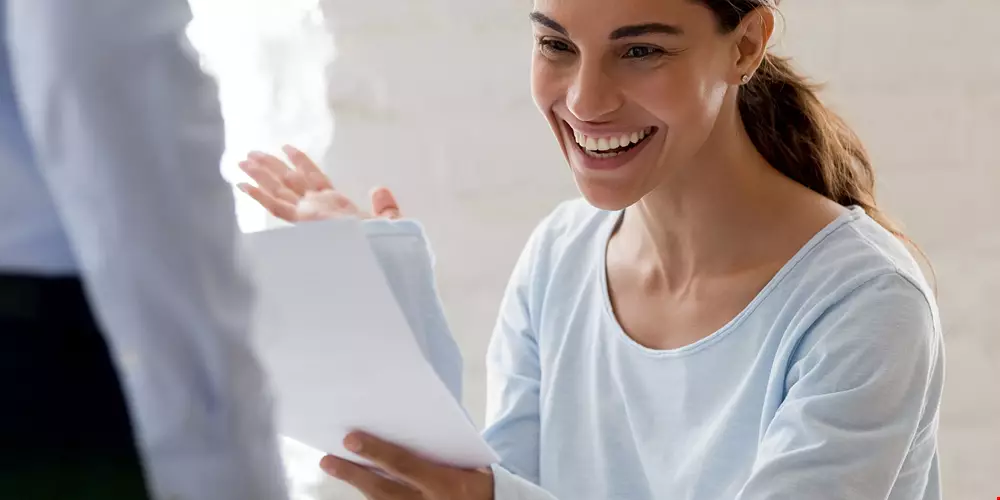 En kvinna tittar på ett papper och ser glad ut, kanske fått ett bra besked Akavia Aspekt