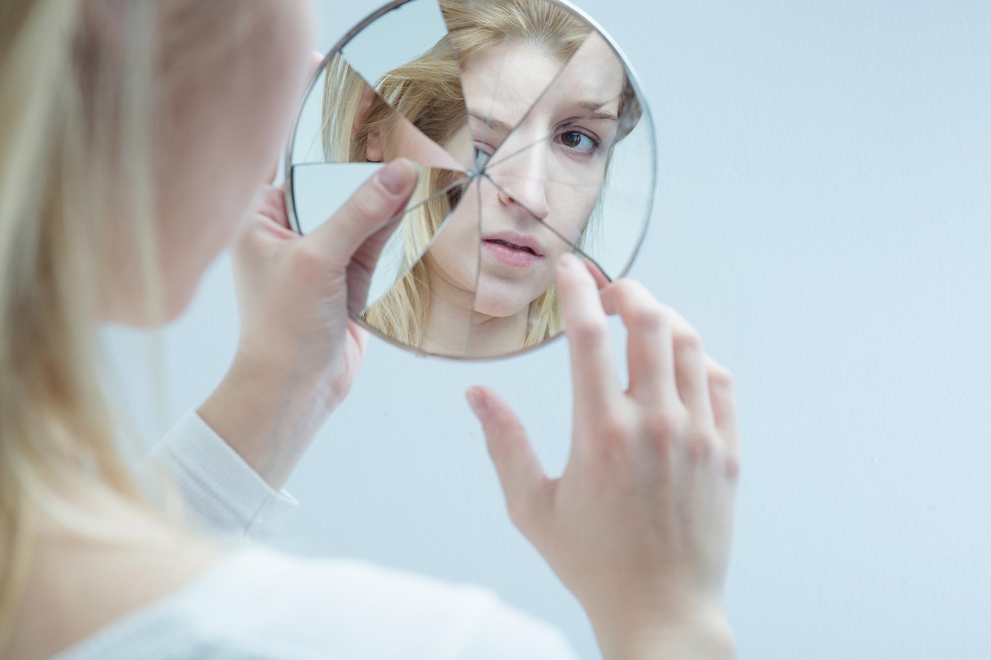 kvinna tittar på sig själv i en spegel som är spräckt, spegelbilden blir förvrängd Akavia Aspekt