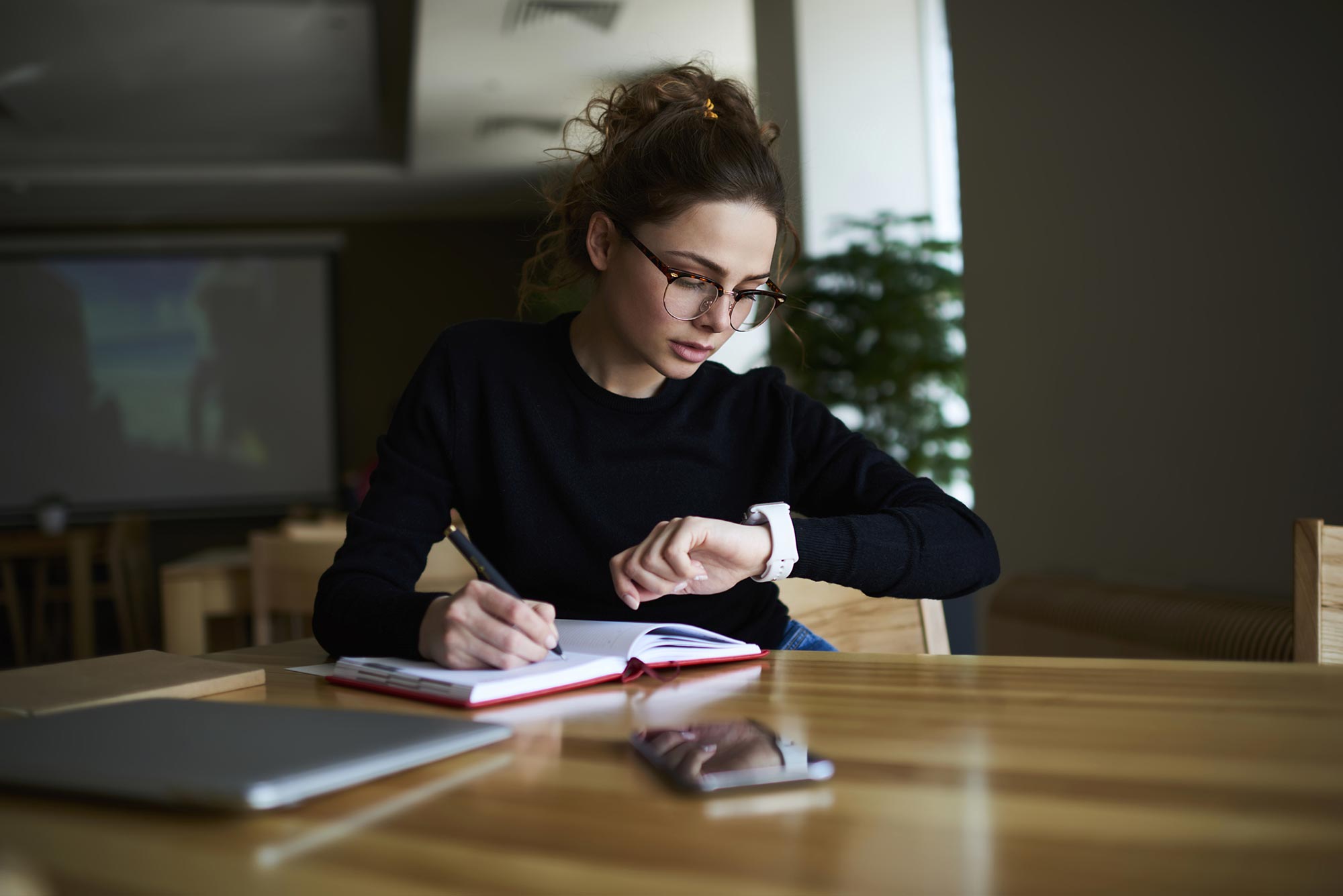 Ung kvinna student skriver i en almanacka tittar på klockan