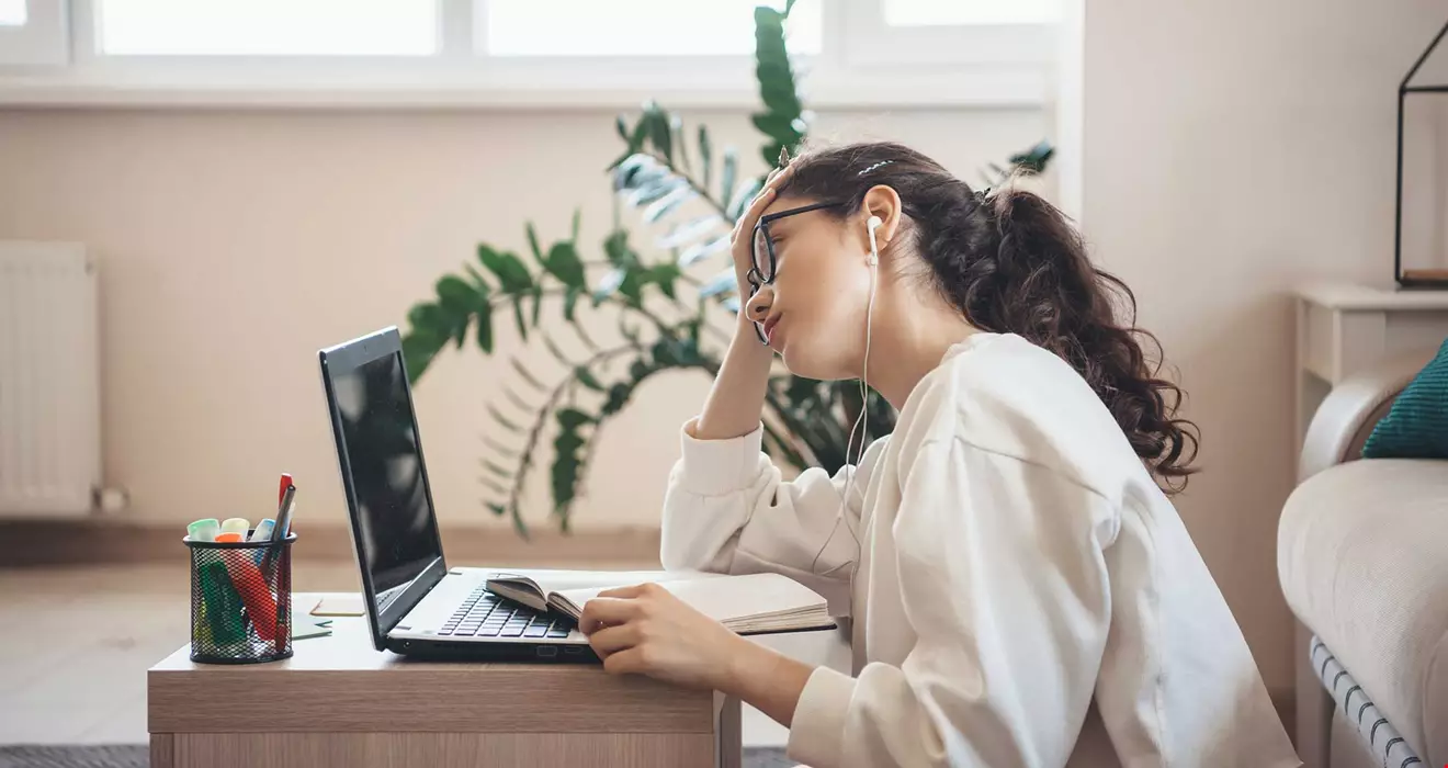 En kvinna med mörkt långt hår sitter framför en dator och ser uttråkad ut, hon lutar huvudet i handen och åt sidan.