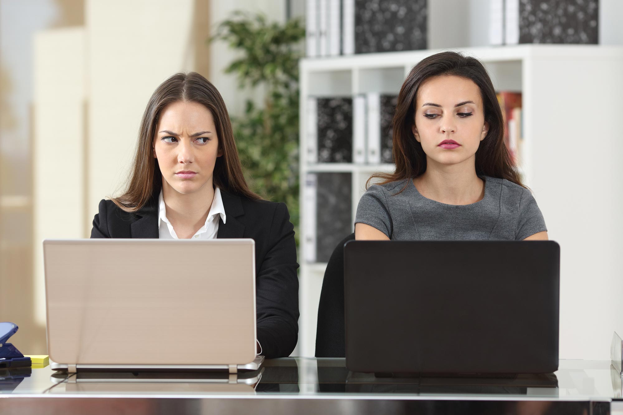 Två kvinnliga kollegor bredvid varandra på kontoret, ser mycket missnöjda ut med varandra, är troligen avundsjuka Akavia Aspekt