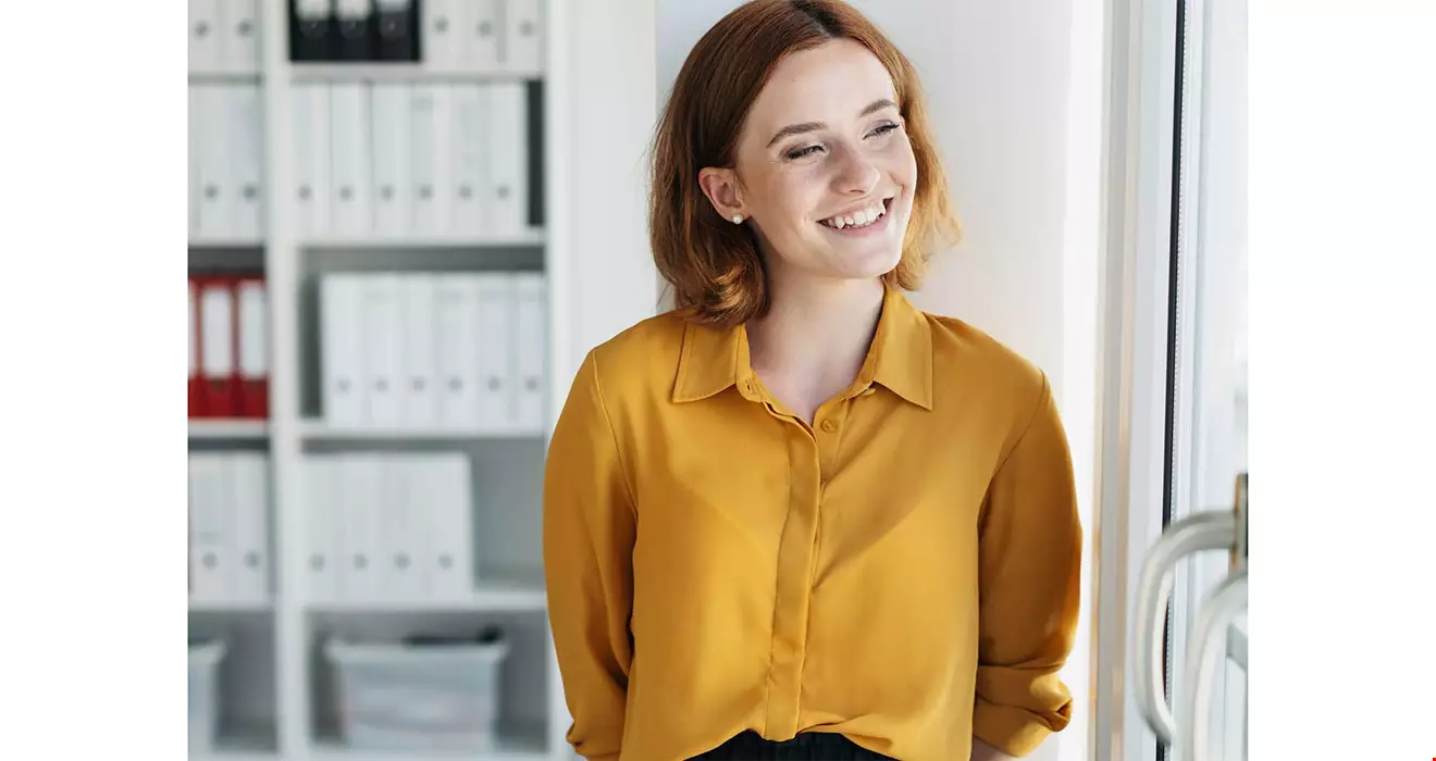 En ung kvinna i kontorsmiljö, hon har gul blir och rött hår Akavia Aspekt