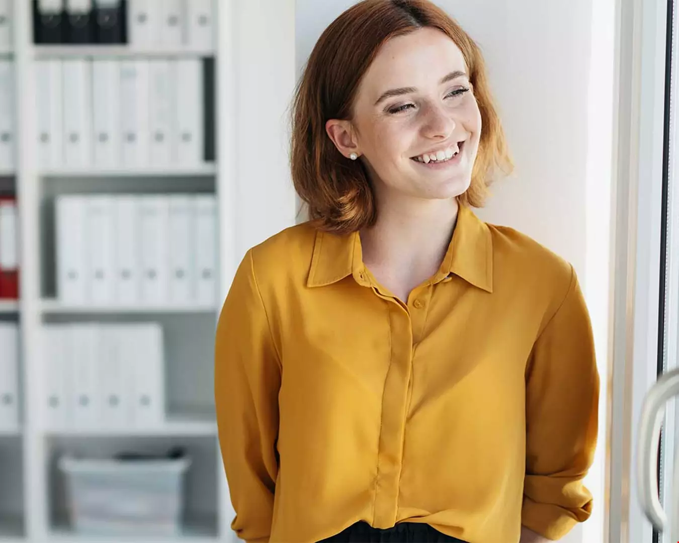 En ung kvinna i kontorsmiljö, hon har gul blir och rött hår Akavia Aspekt