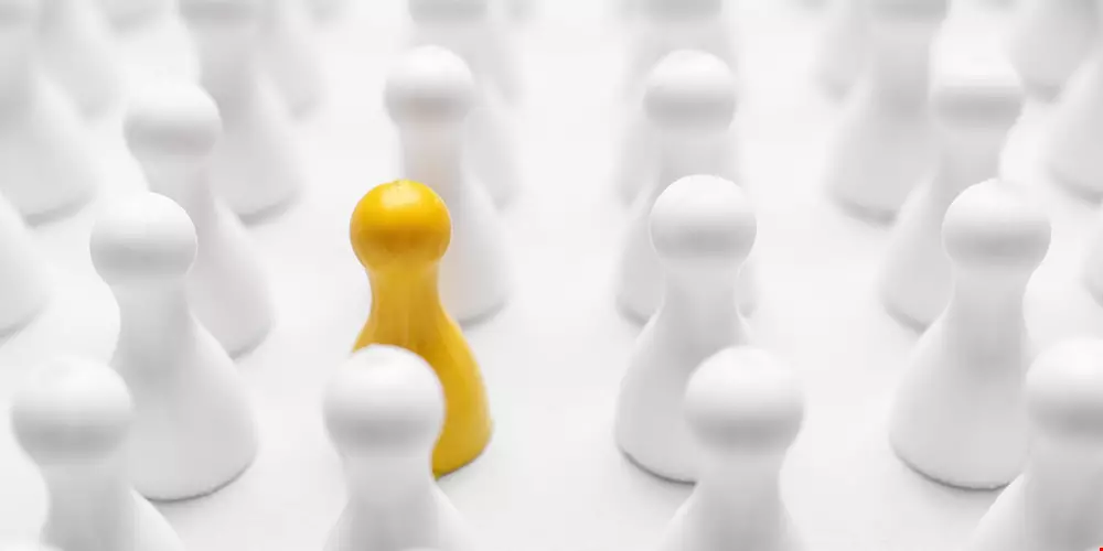 Schackpjäser i vitt med en pjäs i gult som symboliserar att gå sin egen väg, dvs självledarskap 