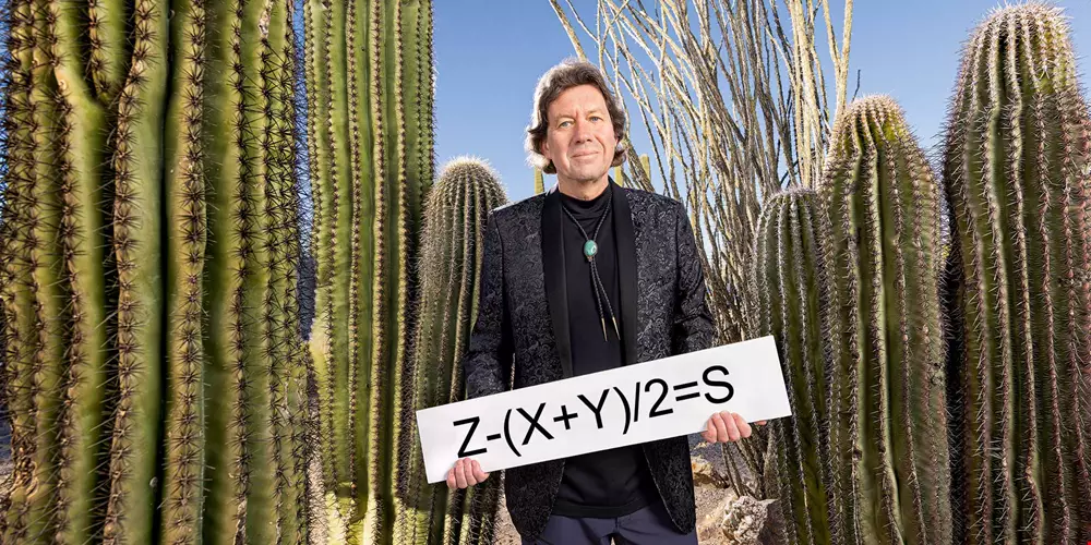 Porträtt Martin Dufwenberg i kavaj bland kaktusar i Arizona-öknen håller i skylt som säger Z-(X+Y)/2=S